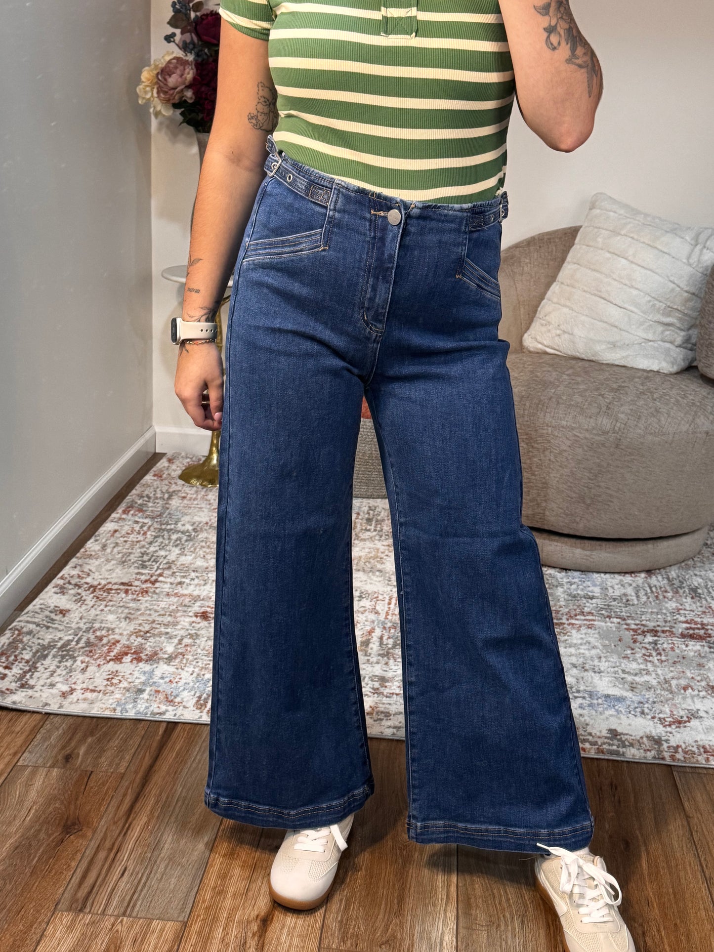 Person wearing blue jeans standing on a wooden floor with a patterned rug.