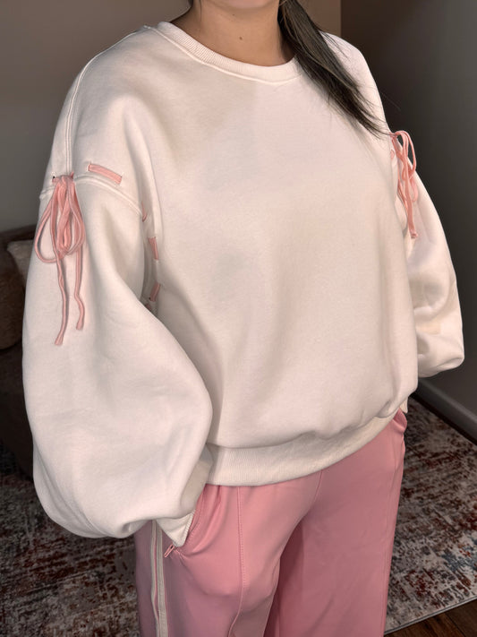 Person wearing a white sweatshirt with pink graphics and pink pants in a room.