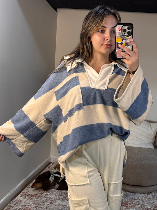 Woman taking a mirror selfie wearing a striped sweater and beige pants in a room.