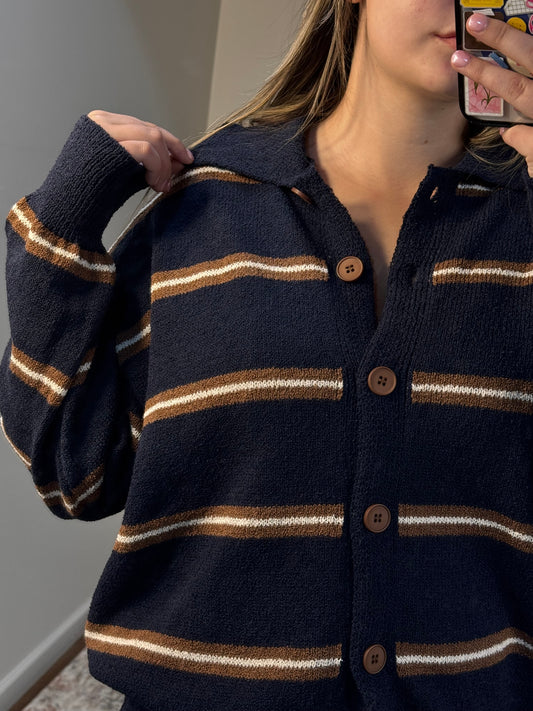 Navy cardigan with gold stripes worn by a person, blurred background