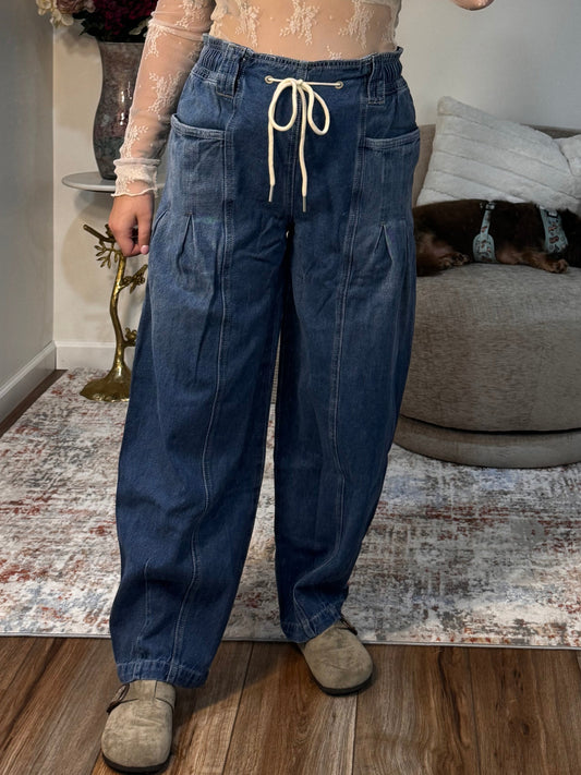 Person taking a mirror selfie wearing a beige top and blue jeans in a room with a cat tree and rug.