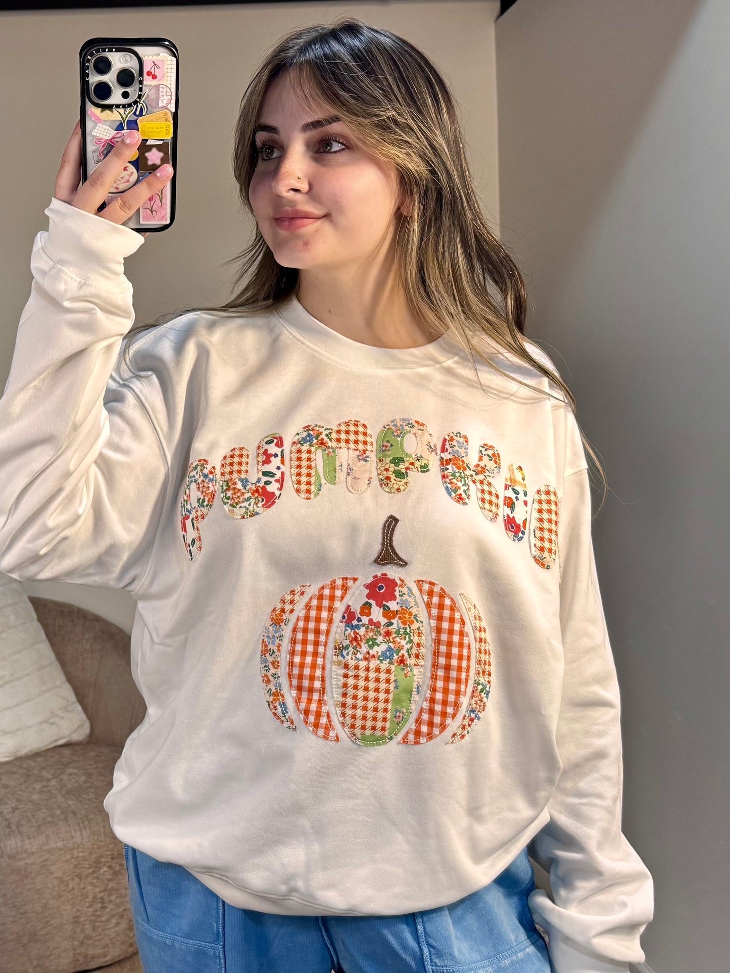 Person wearing a white sweatshirt with a colorful pumpkin design and text.