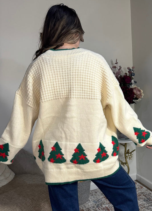 Person wearing a cream sweater with Christmas tree patterns in a room.