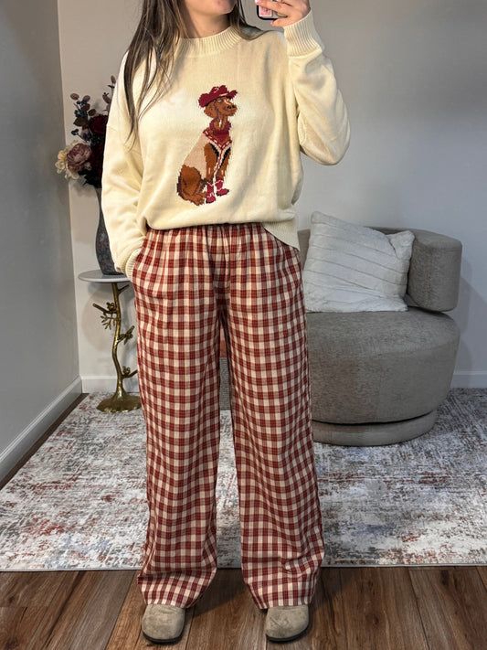 Person wearing a cream-colored hoodie with floral designs and red plaid pants in a room.