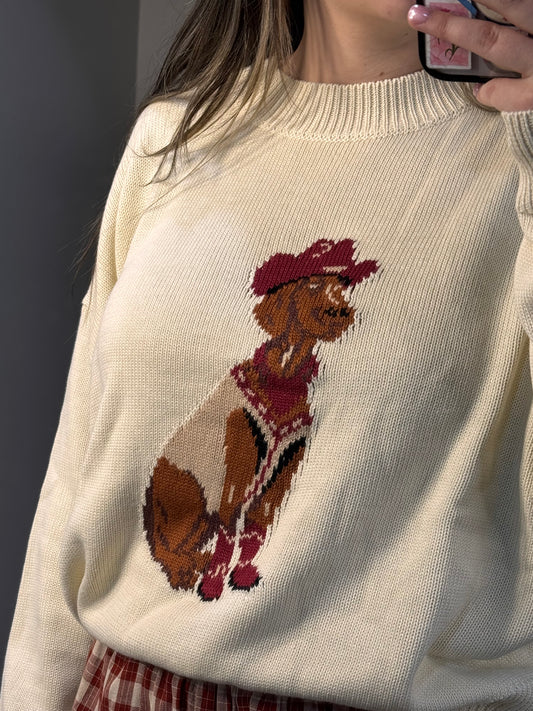 Close-up of a beige sweater with embroidered design on a plain background