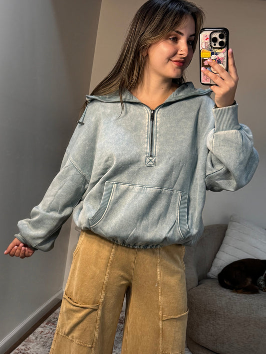 Person wearing a denim jacket and tan pants standing in a room with a couch and rug.