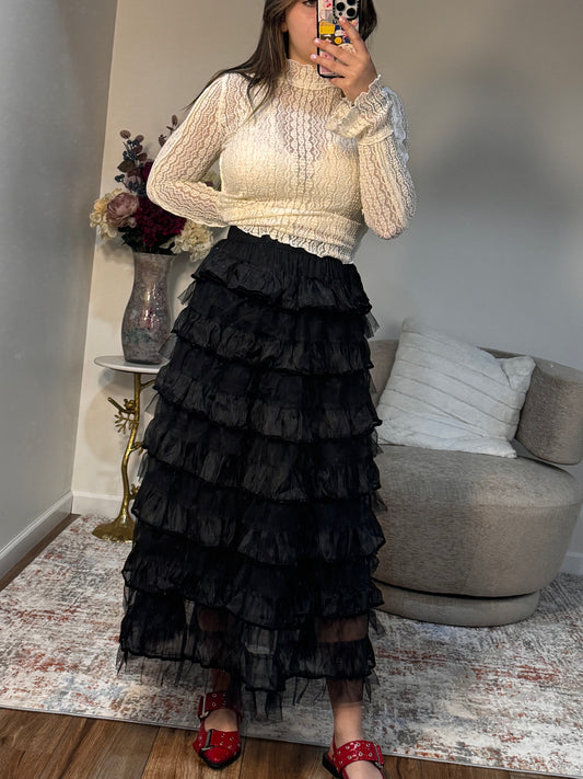 Woman wearing a cream sweater and black ruffled skirt in a living room setting.