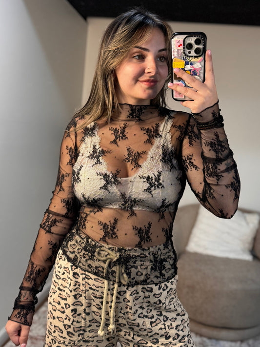 Person wearing a sheer top with floral patterns and leopard print pants in a room.