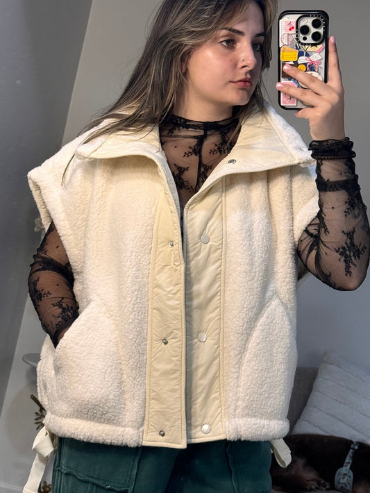 Person wearing a cream-colored jacket in a room with a couch and pillows.