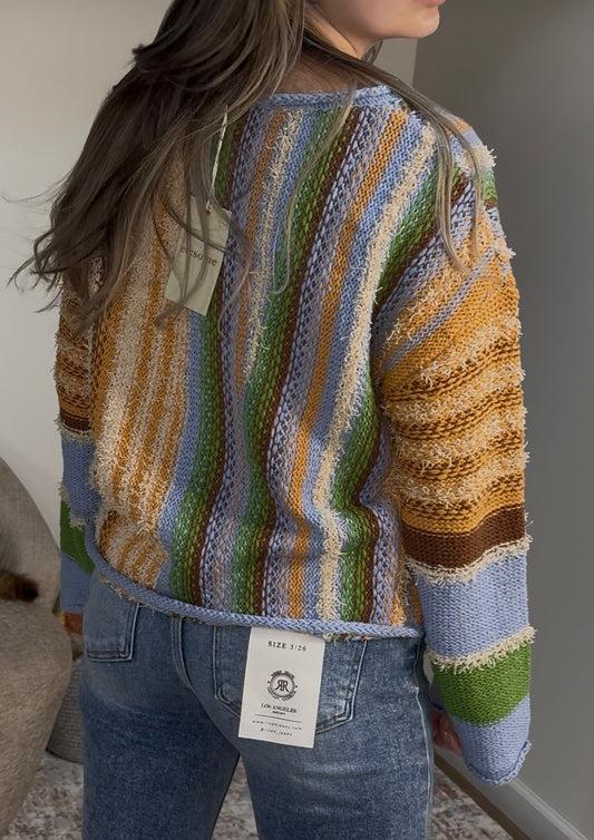 Person wearing a colorful striped sweater with a visible tag, standing indoors.