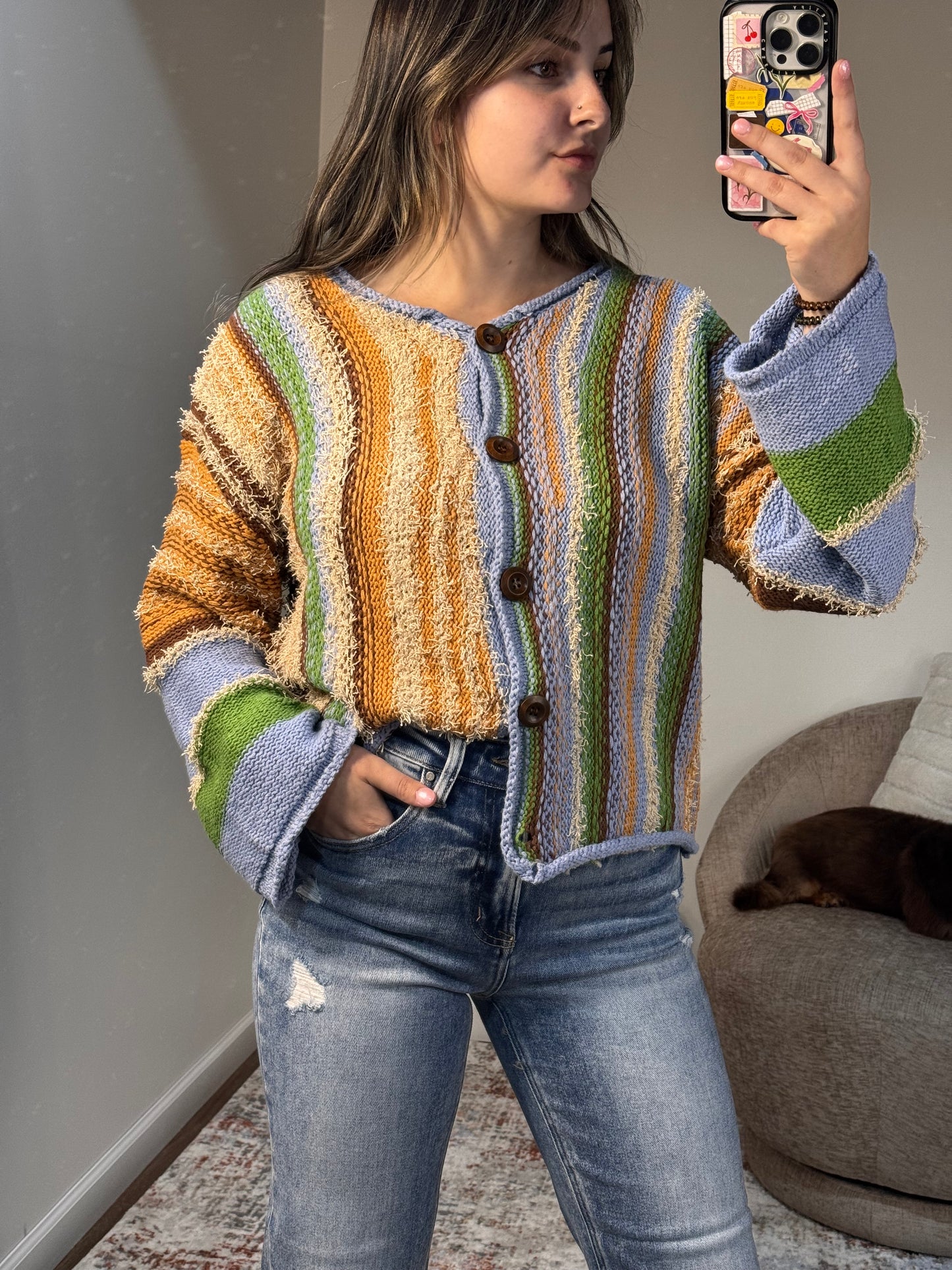Person wearing a colorful striped sweater and jeans, taking a mirror selfie.
