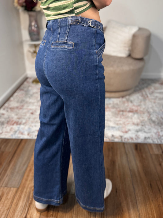 Person wearing blue jeans and a striped shirt in a room with wooden flooring and a rug.