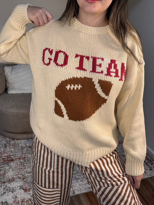 Person wearing a cream sweater with a football design and 'GO TEAM' text.