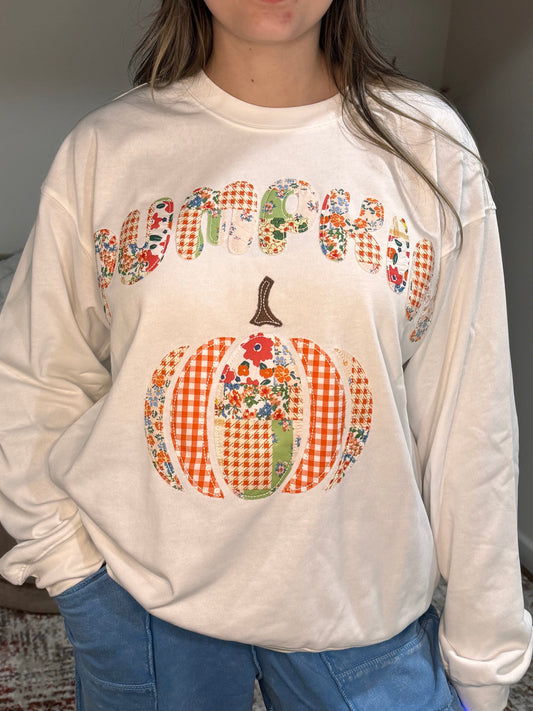 Person wearing a cream sweatshirt with a colorful pumpkin design and 'pumpkin' text.