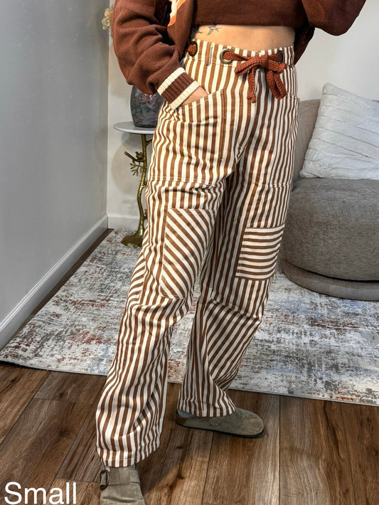 Person wearing brown and white striped pants with a brown top in a room.