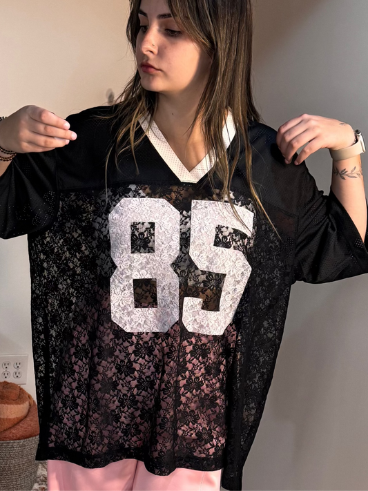 Person wearing a black lace garment with the number 85 on it, indoors.