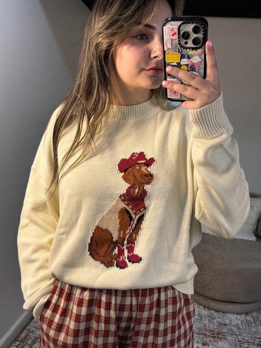 Person wearing a cream sweater with a dog design, holding a phone.