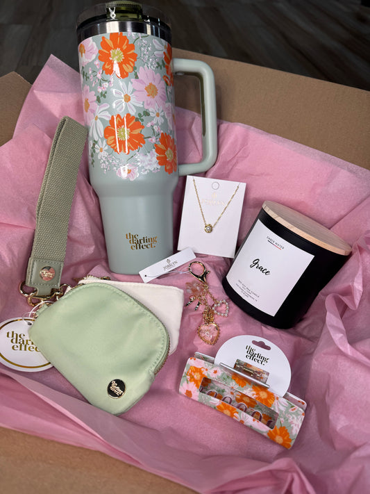 Gift items including a floral thermos, pouch, and other decorative items on pink tissue paper.