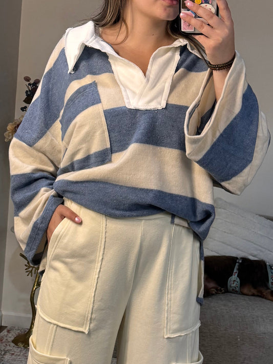 Person wearing a striped sweater and beige pants taking a mirror selfie.