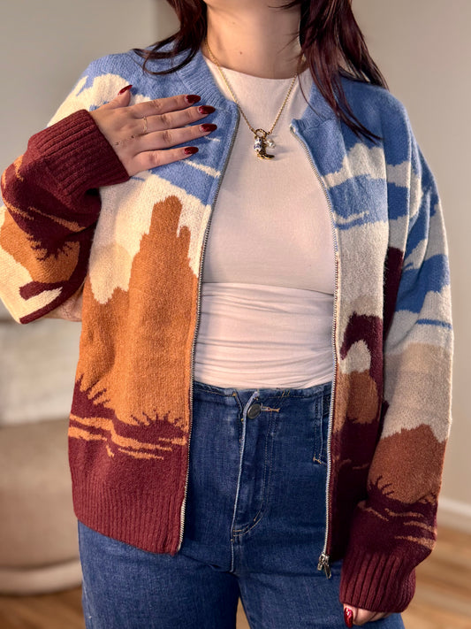 A multi-color bomber sweater with a desert motif jacquard pattern, round neck, and zipper closure.
