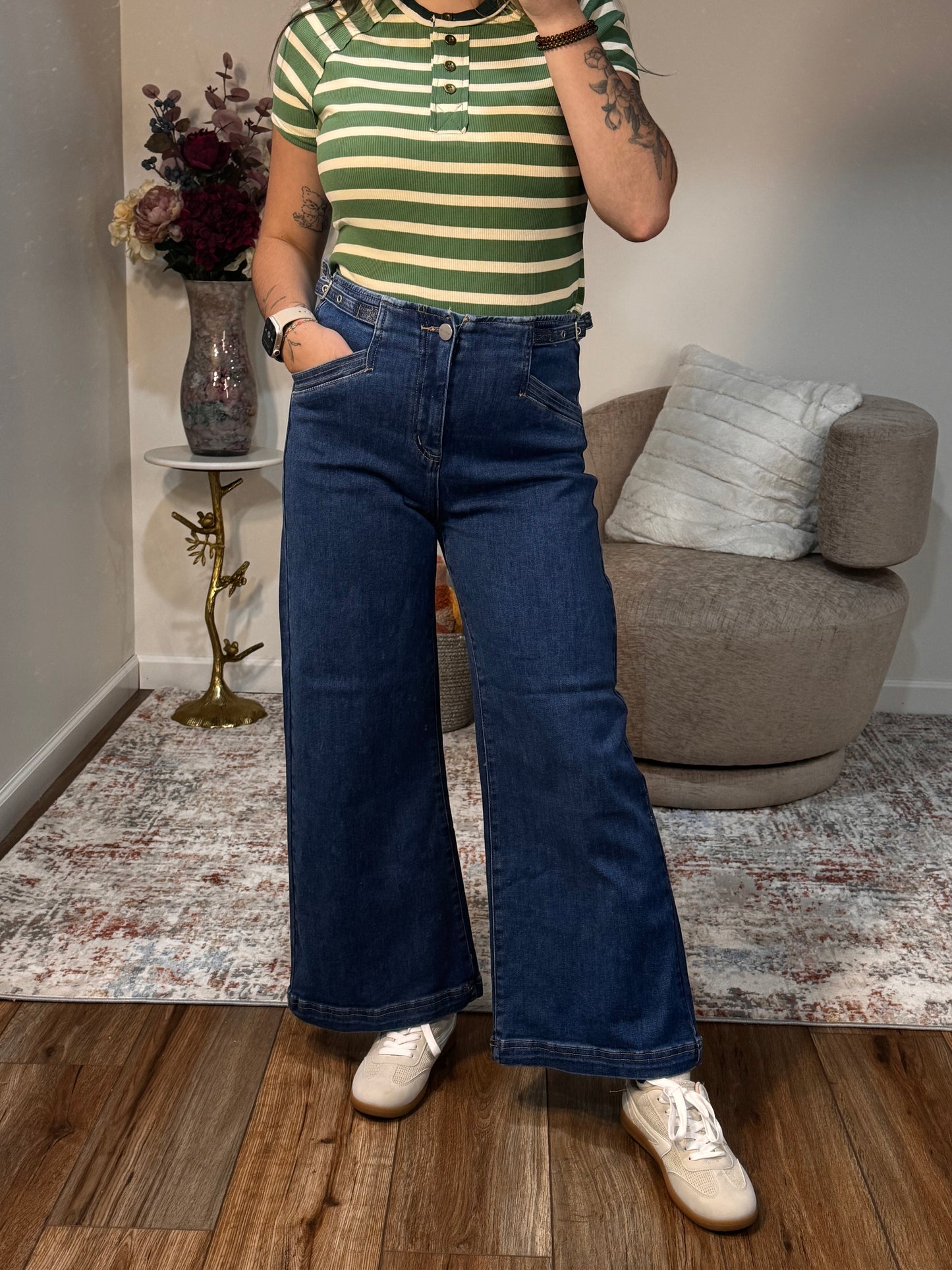 Person wearing a striped shirt and blue jeans standing in a living room.