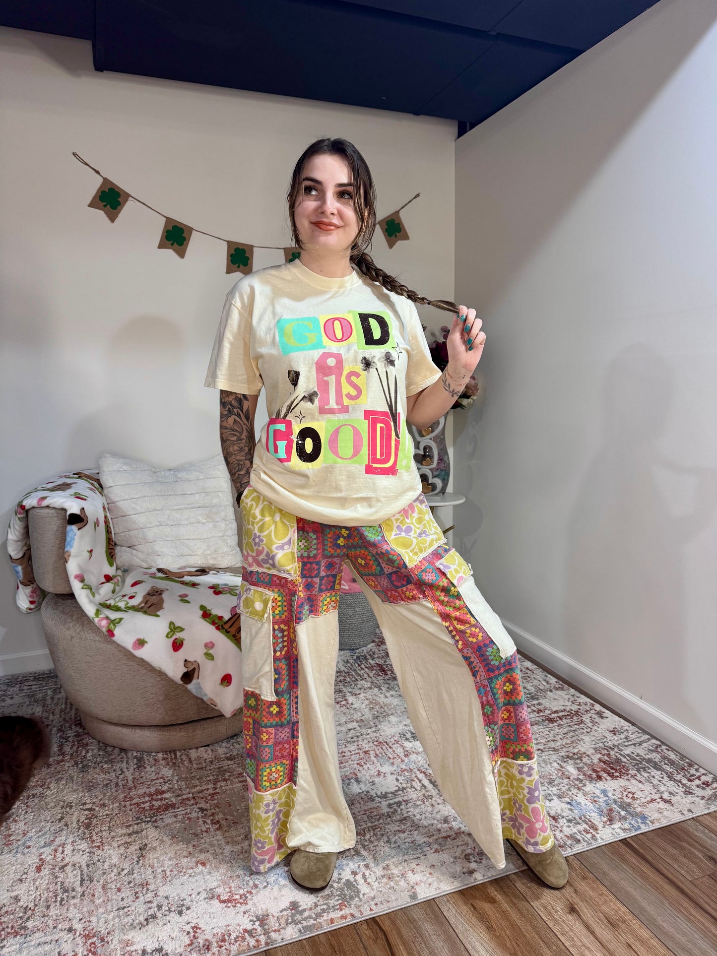 Person wearing a colorful 'GOD IS GOOD' t-shirt and patterned pants in a room.