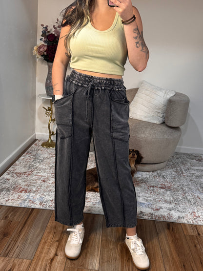 Person wearing a yellow top and black pants standing in a room with a couch and rug.
