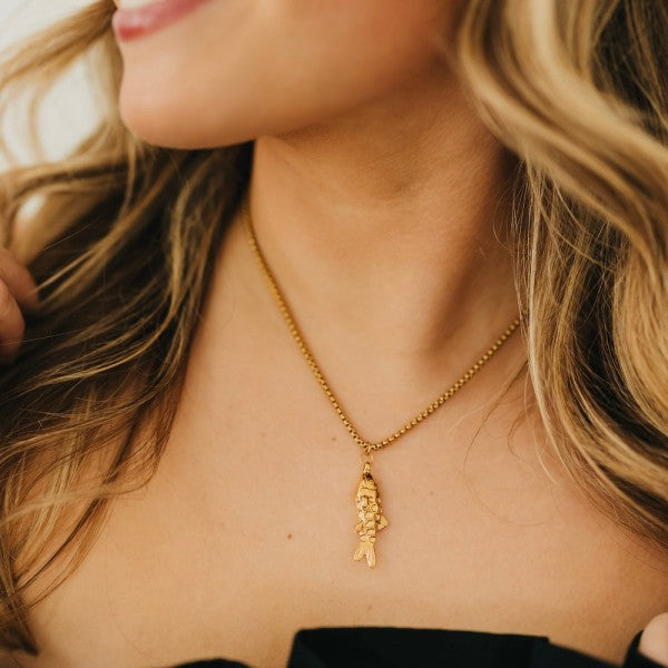 Gold pendant necklace with a fish design worn by a person.