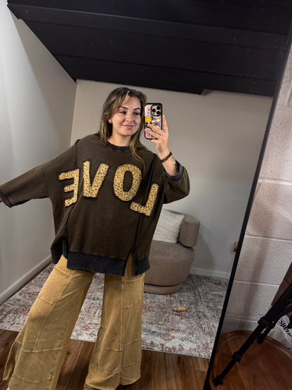Person wearing a brown sweatshirt with 'LOVE' printed in leopard letters