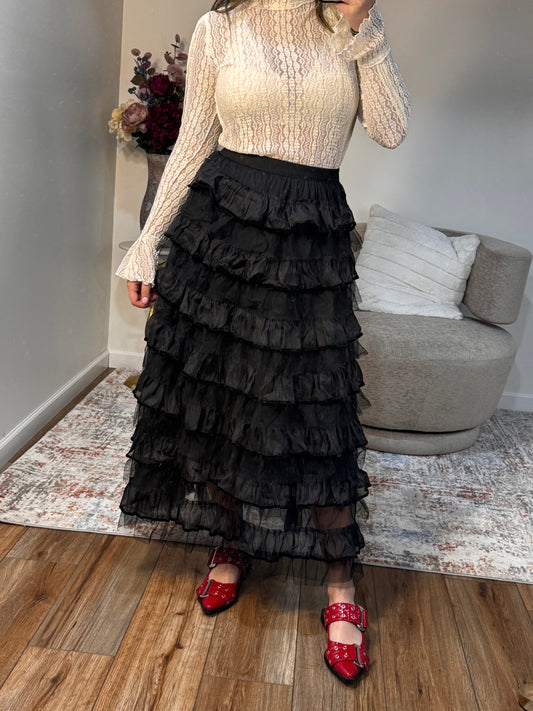 Person wearing a black ruffled skirt standing in a room with a gray sofa and wooden floor.