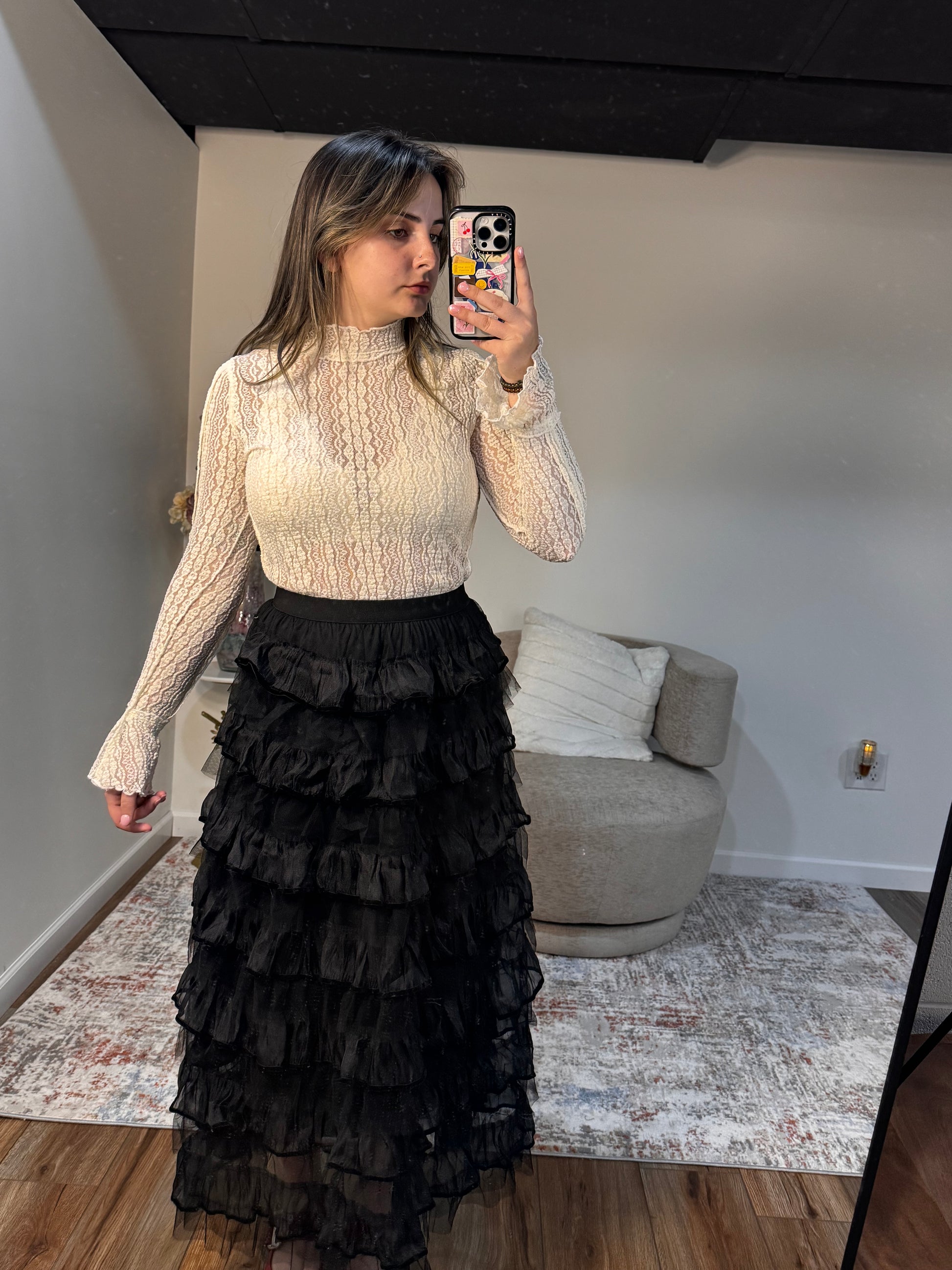 Person wearing a textured sweater and black ruffled skirt in a room with a sofa and coffee table.
