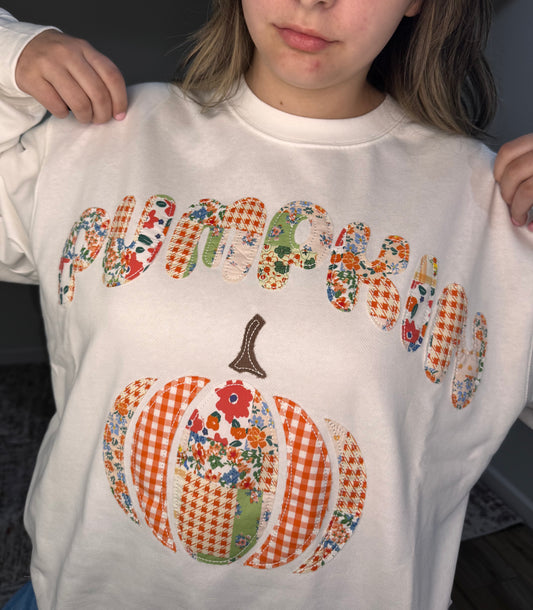 Person wearing a sweatshirt with a colorful 'Pumpkin' design and a checkered pumpkin graphic.