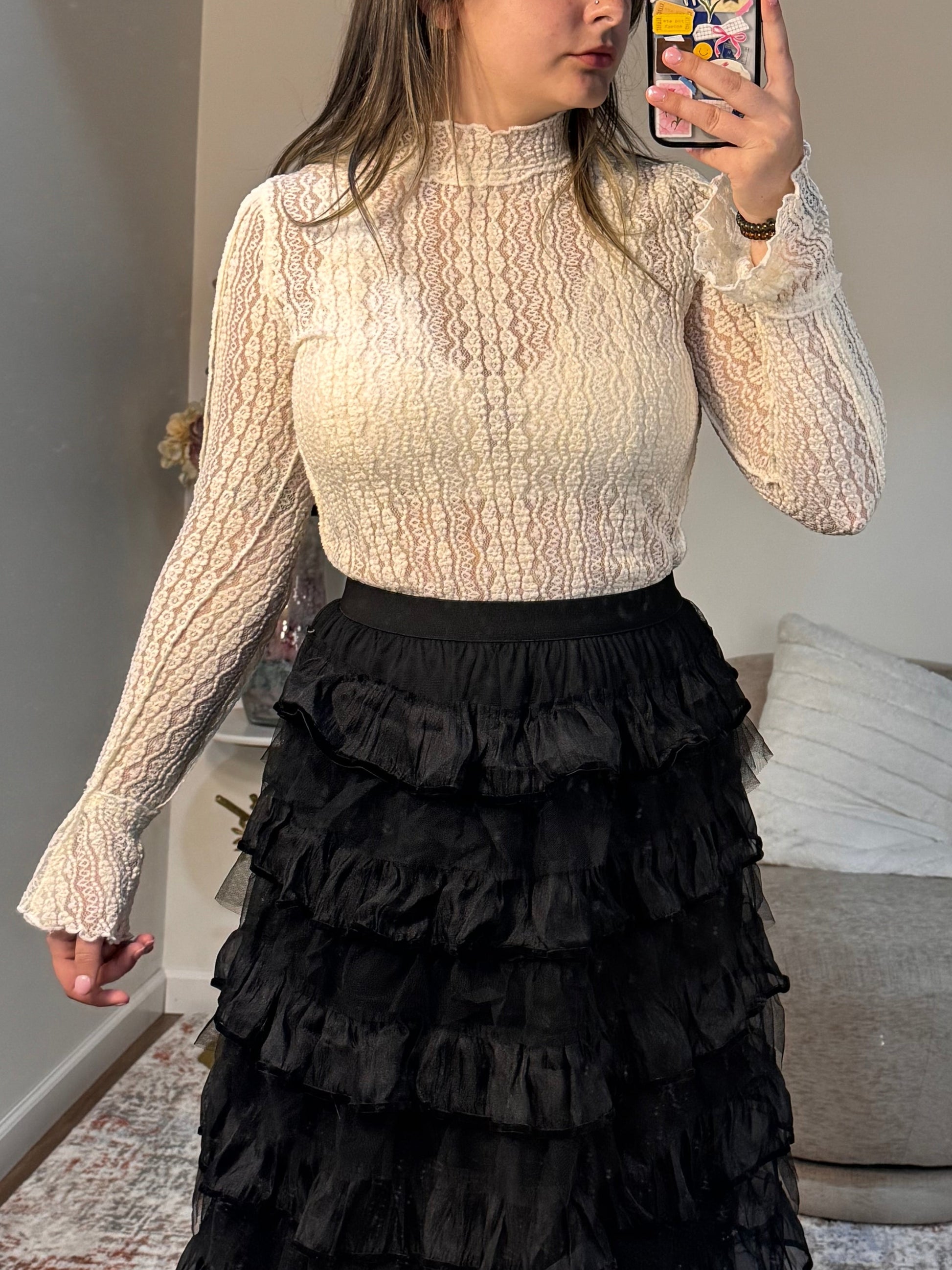 Person wearing a textured shirt and black ruffled skirt in a room with a sofa and coffee table.
