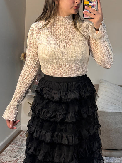 Person wearing a textured shirt and black ruffled skirt in a room with a sofa and coffee table.