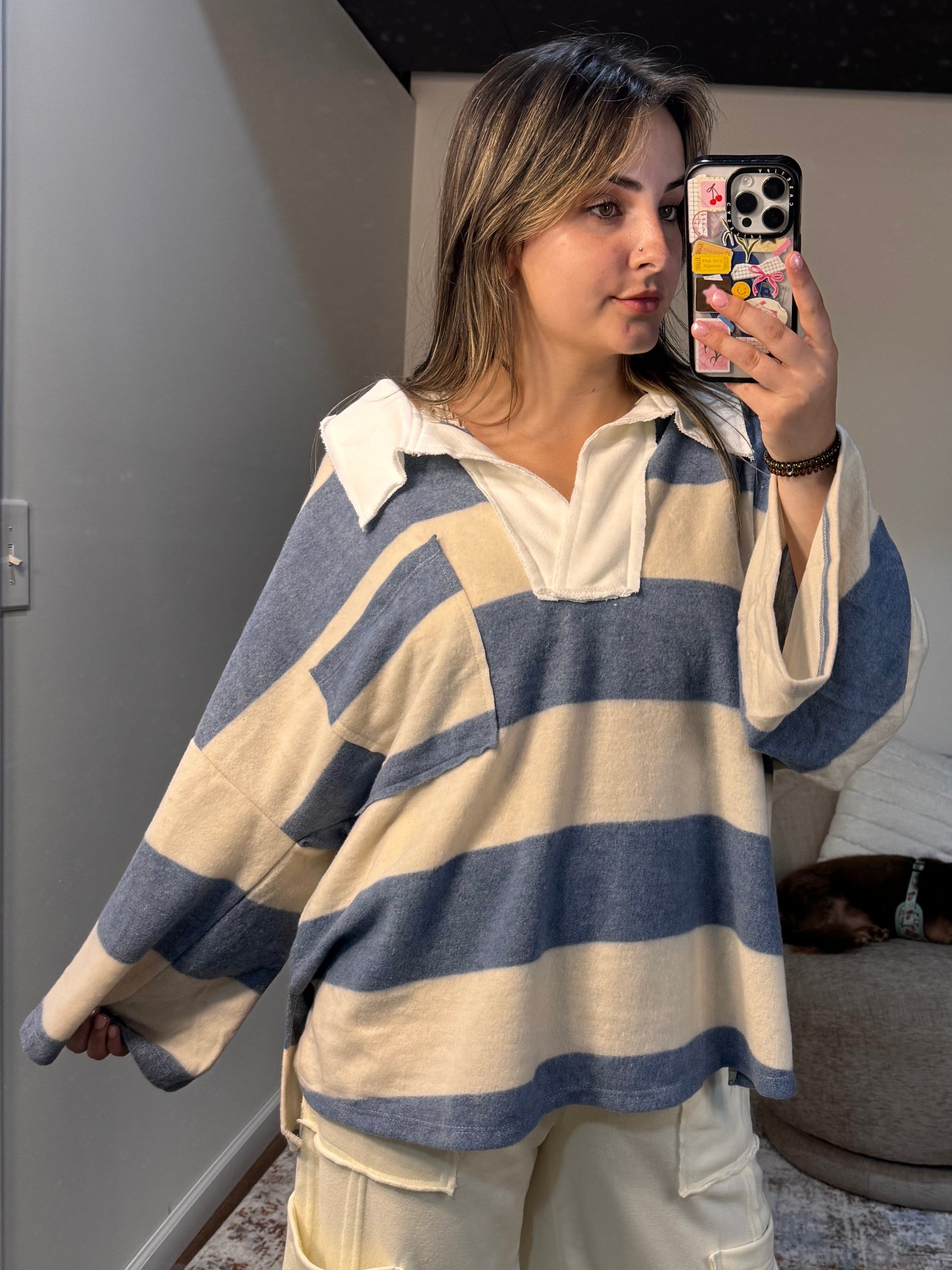 Woman wearing a striped sweater taking a mirror selfie in a room.