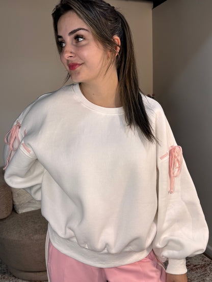 Person wearing a white sweatshirt with pink designs and pink pants in a room.