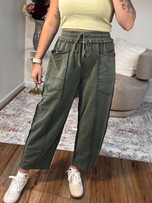 Person wearing green pants and white sneakers standing on a wooden floor.