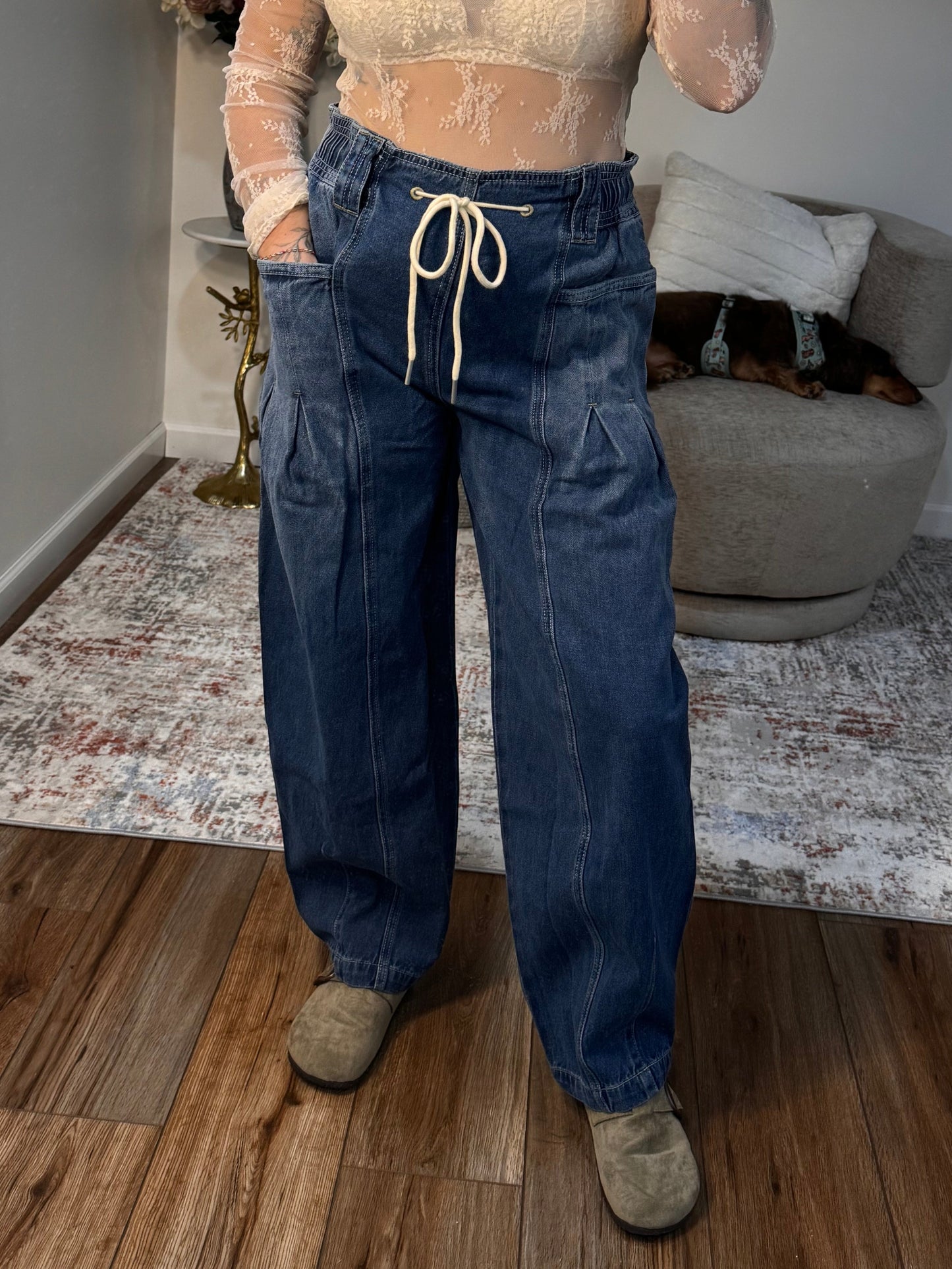 Person taking a mirror selfie wearing a beige top and blue jeans in a room with a sofa and coffee table.