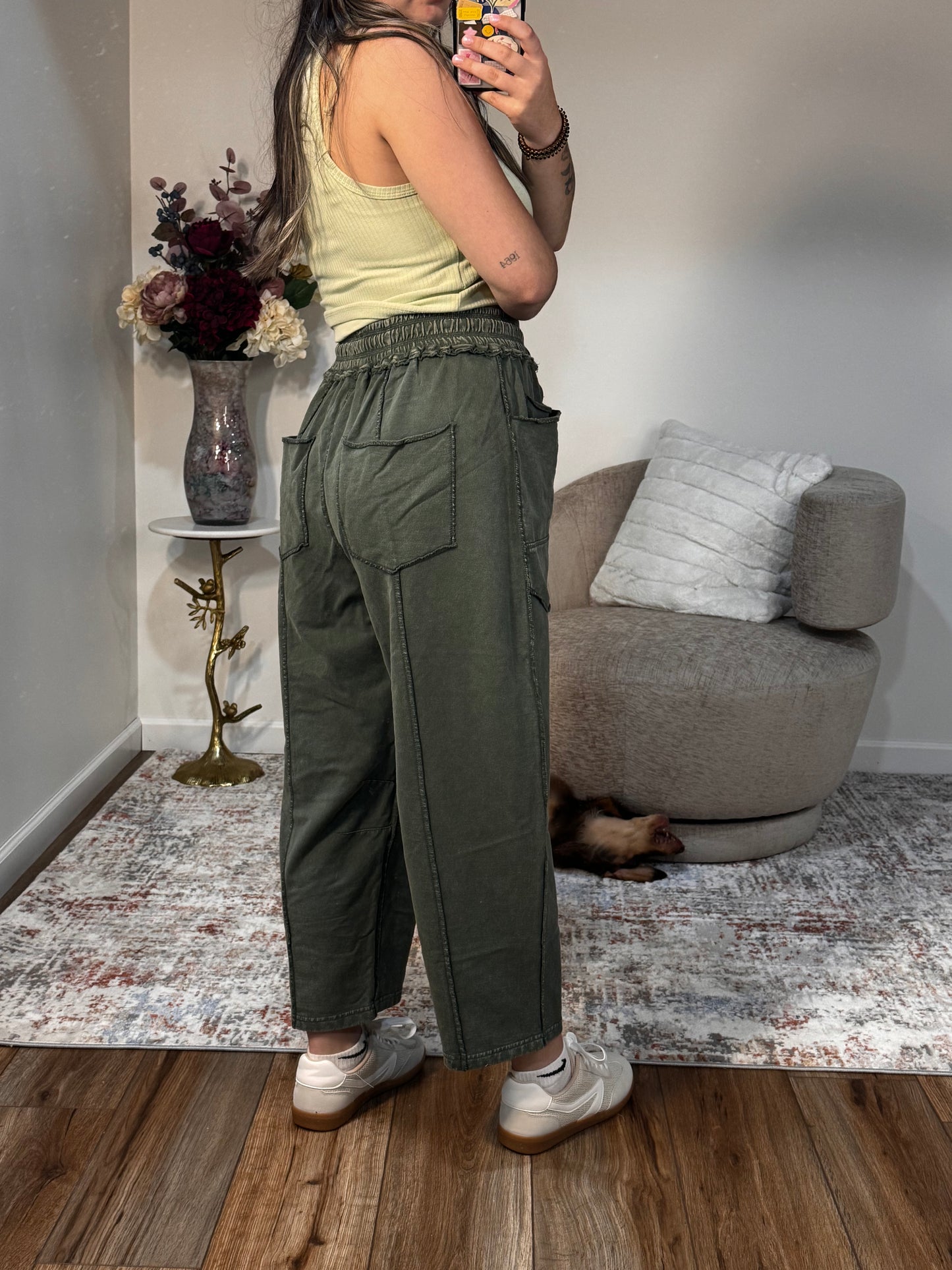 Person wearing green cargo pants standing in a room with a couch and decorative items.