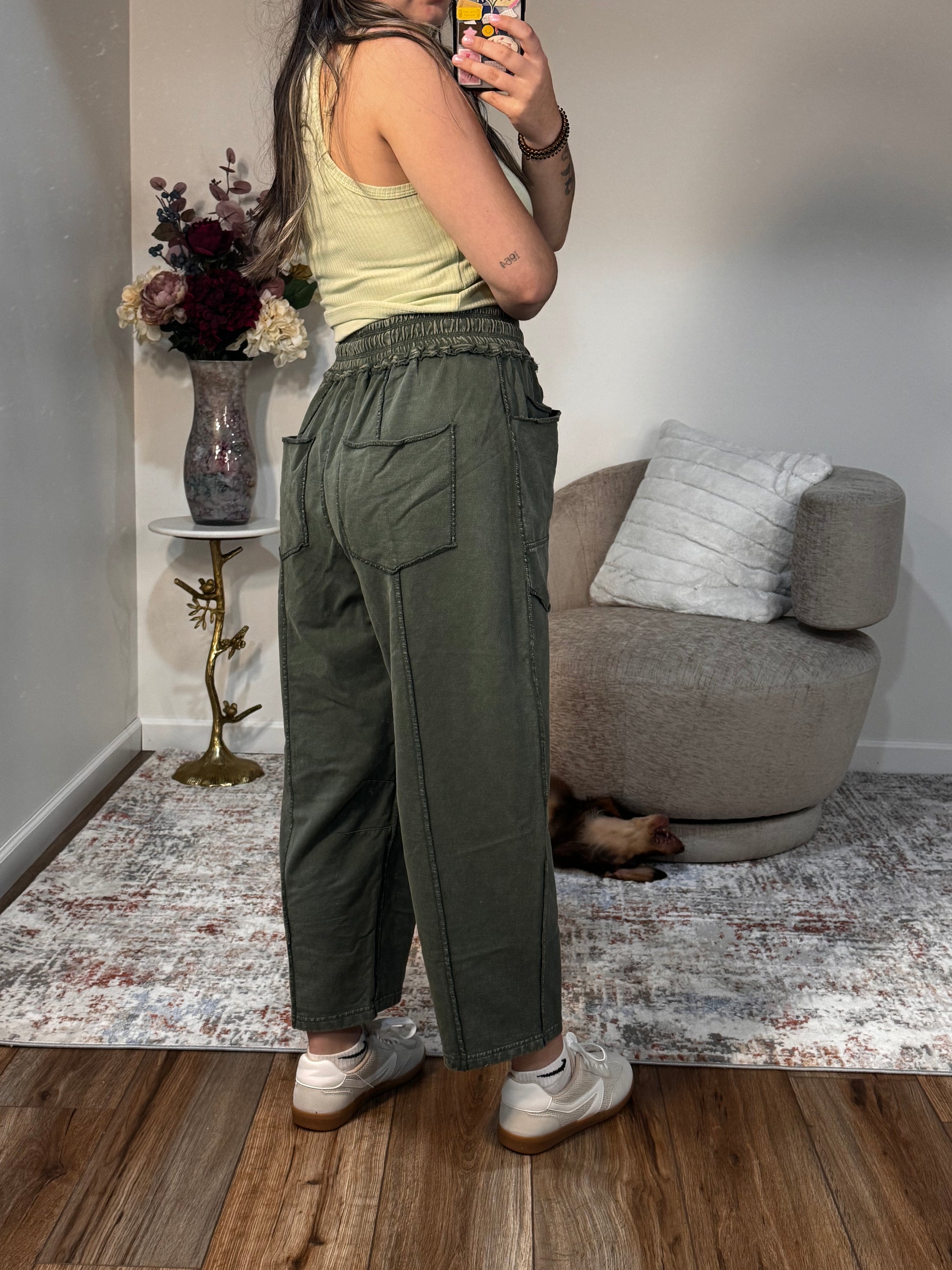 Person wearing green cargo pants standing in a room with a couch and decorative items.