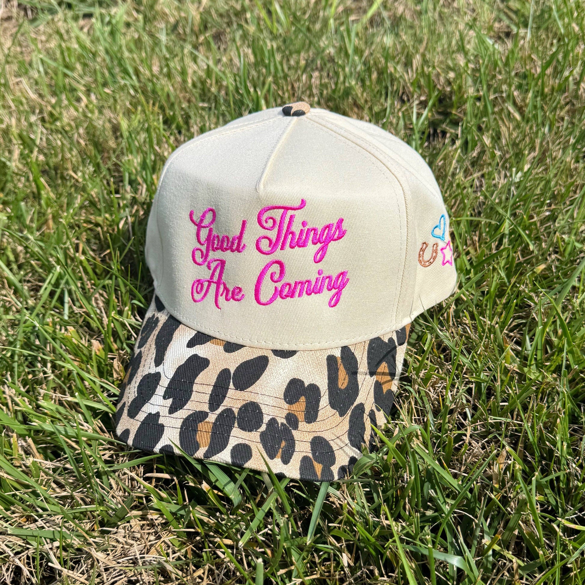 Cap with leopard print brim and 'Good Things Are Coming' text on grass