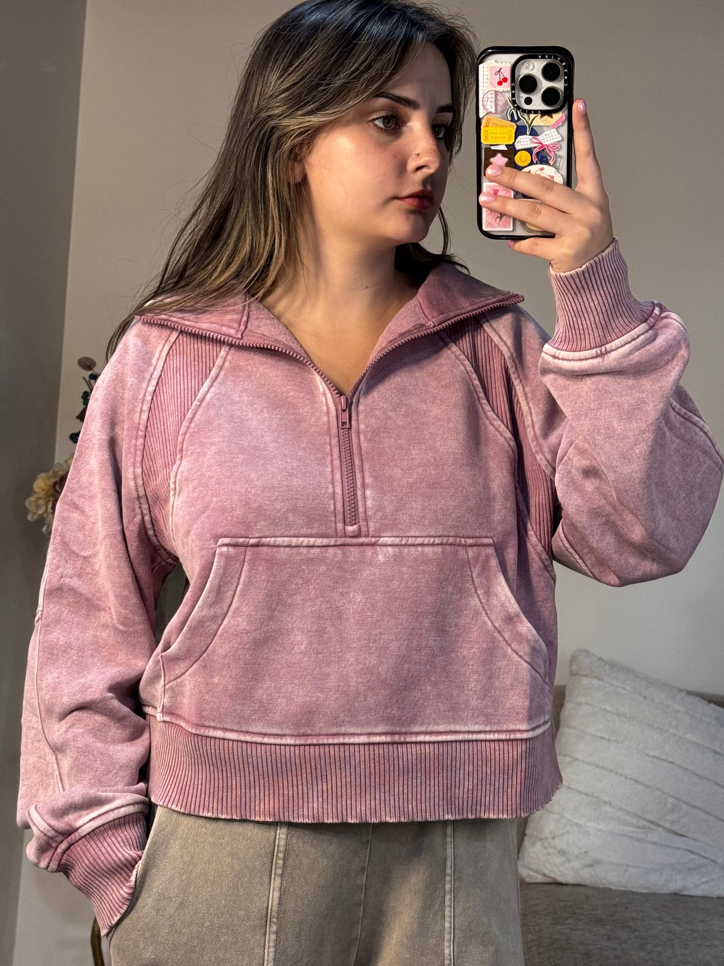 Person wearing a pink jacket taking a mirror selfie in a room.