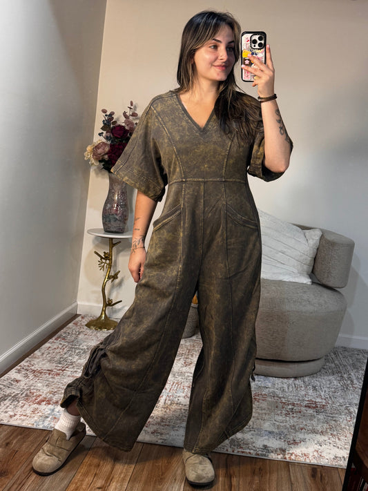 Person wearing a dark green outfit taking a mirror selfie in a room with furniture and decor.
