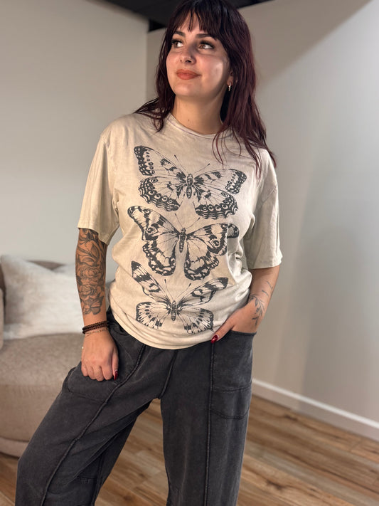 A woman wears a mineral washed stone gray tee with a butterflies graphic, crew neck, and short sleeves.