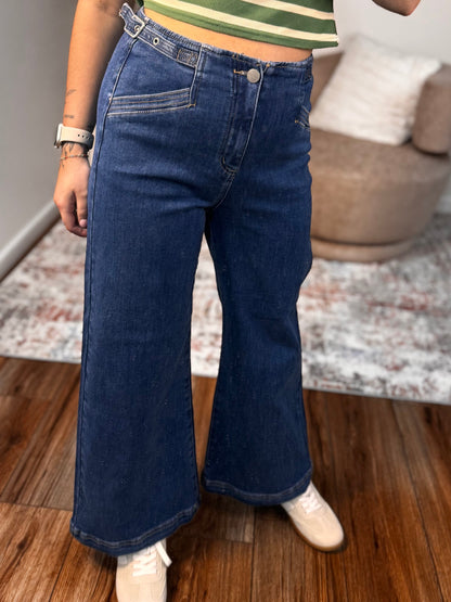 Person wearing a green striped shirt and blue jeans taking a mirror selfie.