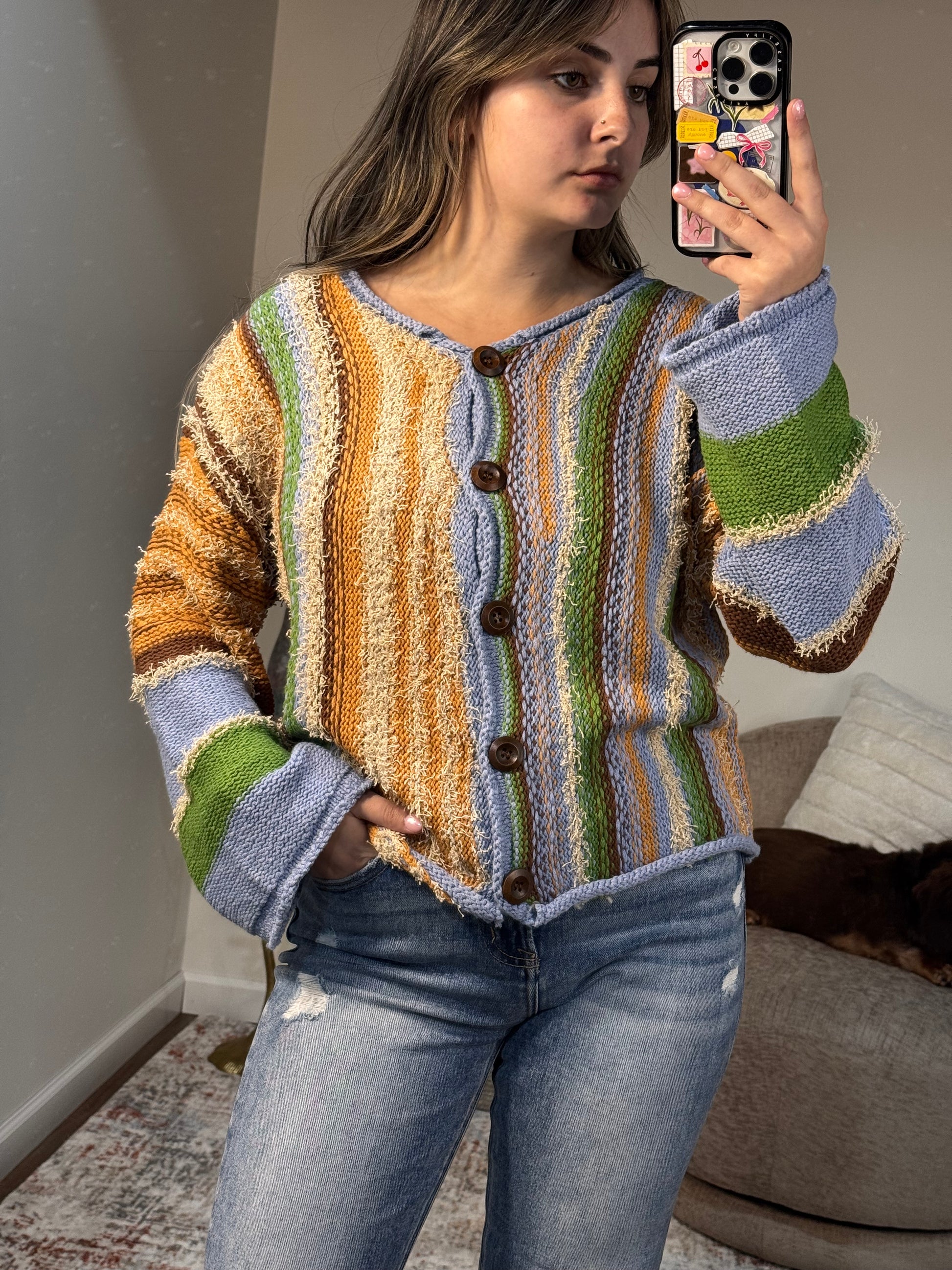 Person wearing a colorful striped sweater taking a mirror selfie.