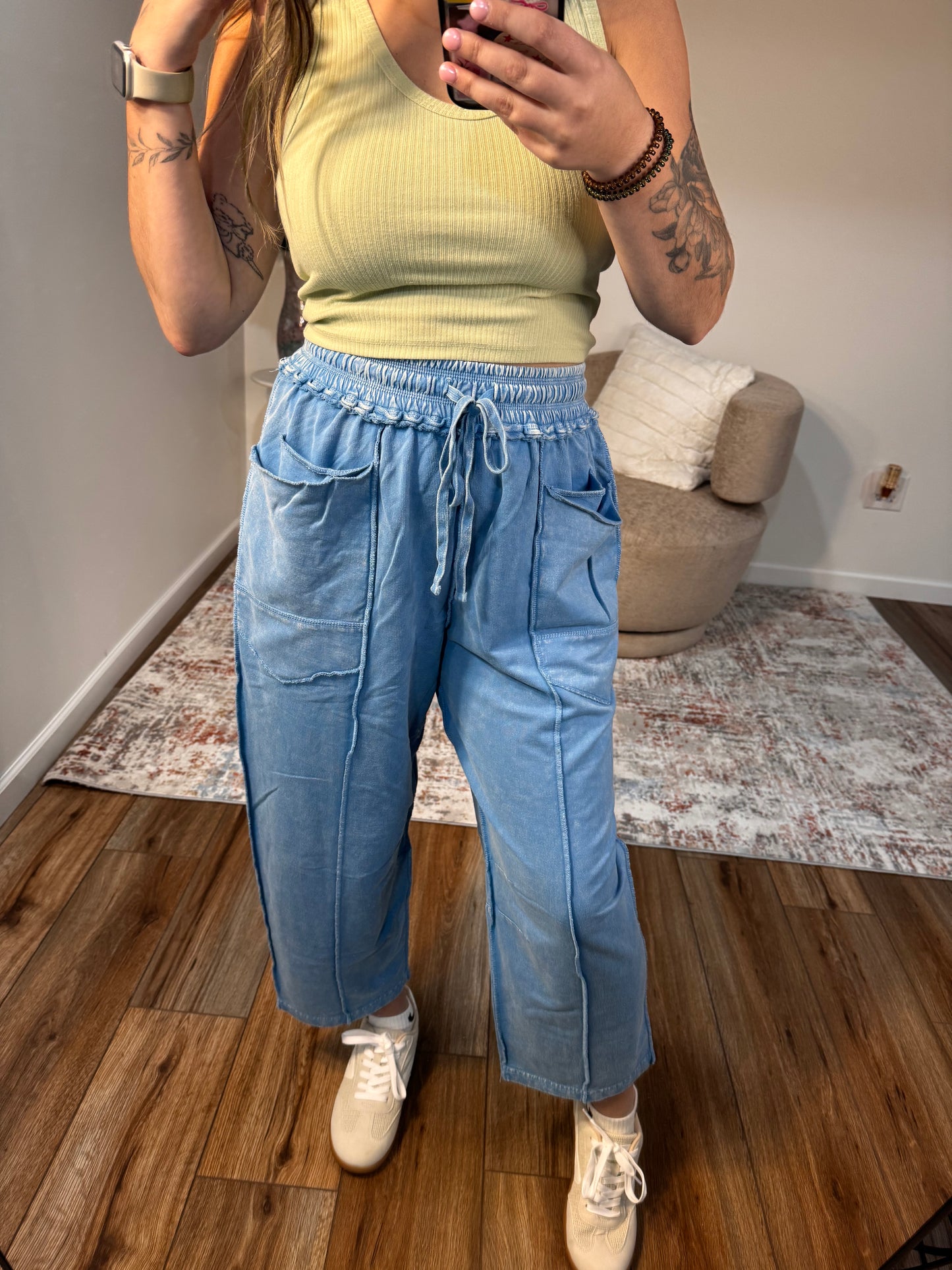 Person wearing a yellow top and blue pants standing on a wooden floor.