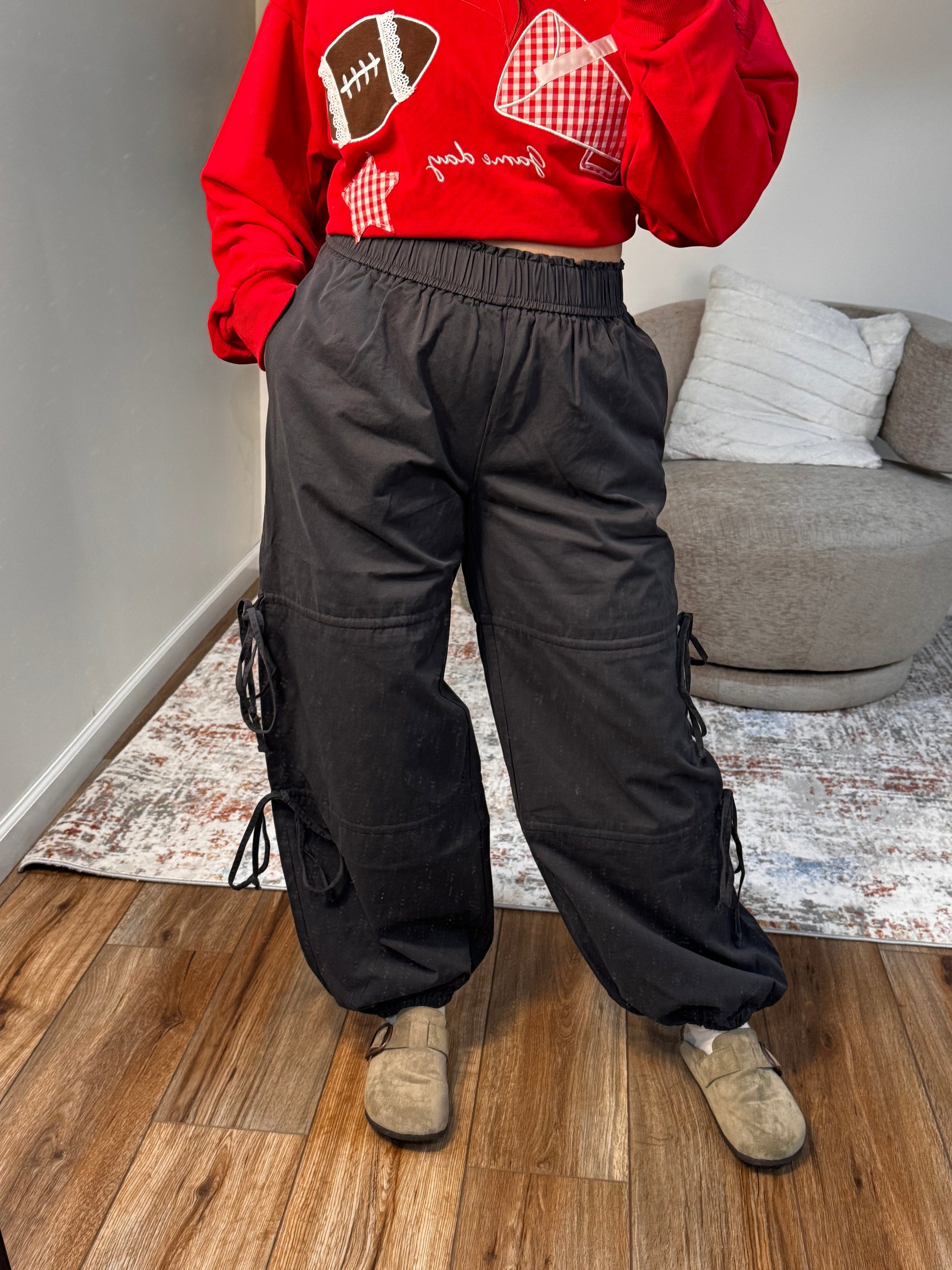Person wearing a red hoodie with a football design and black pants on a wooden floor.