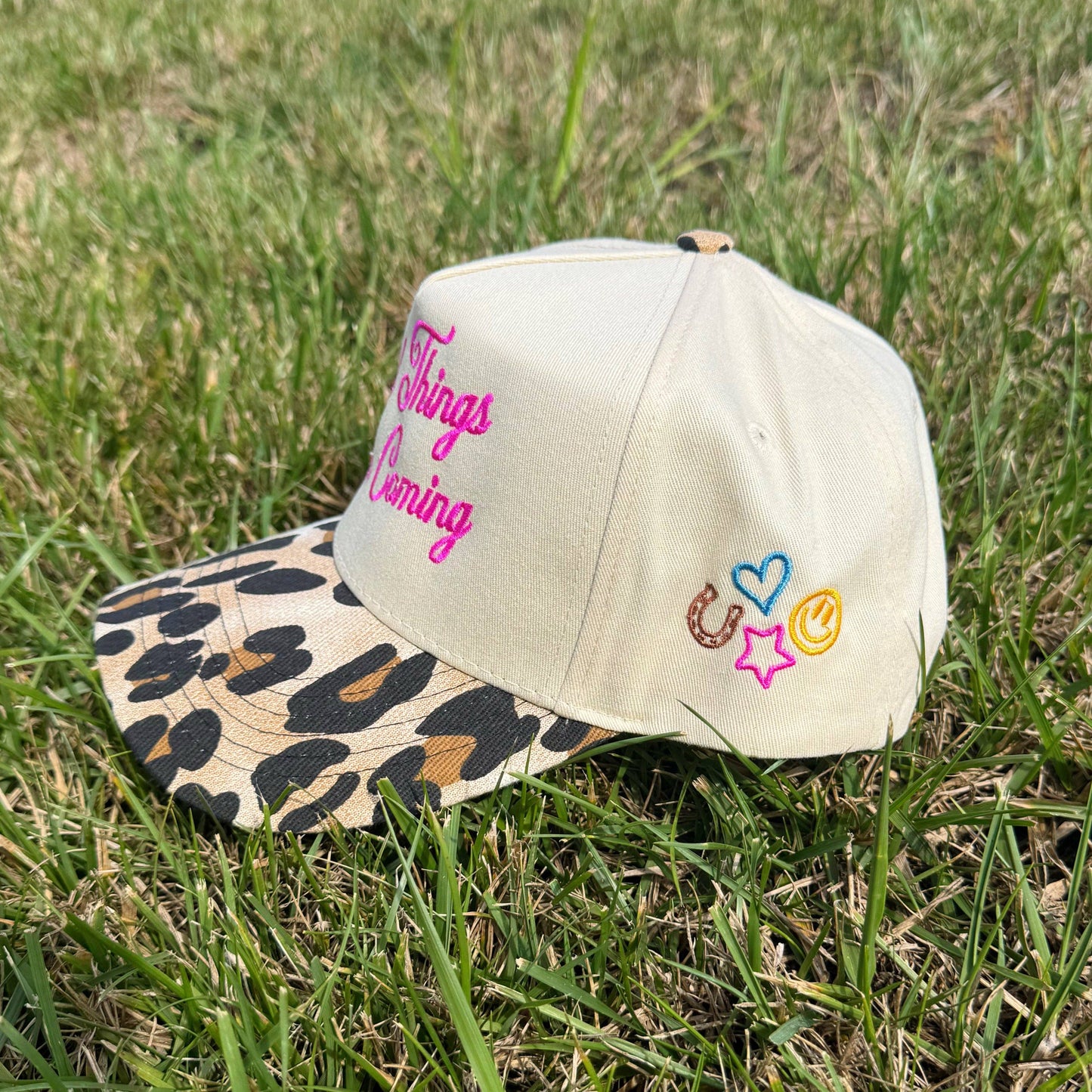 Beige cap with leopard print brim and colorful text and symbols on grass