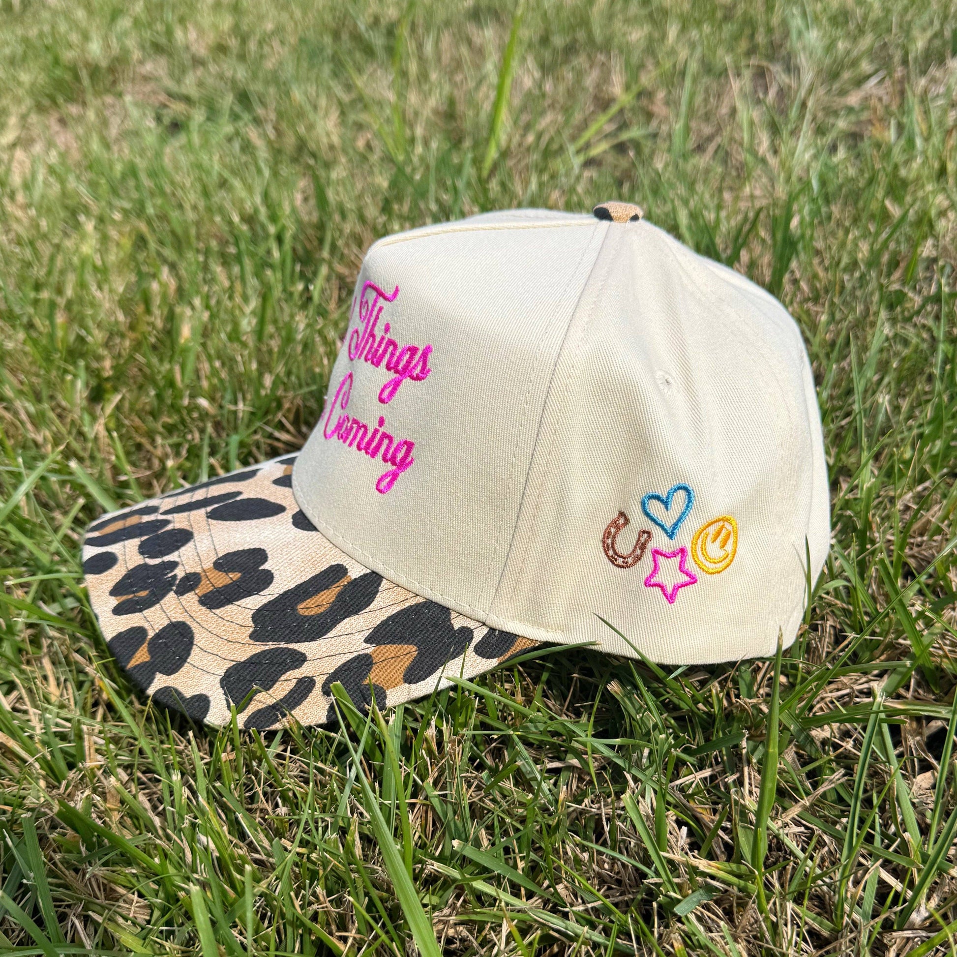 Beige cap with leopard print brim and colorful text and symbols on grass